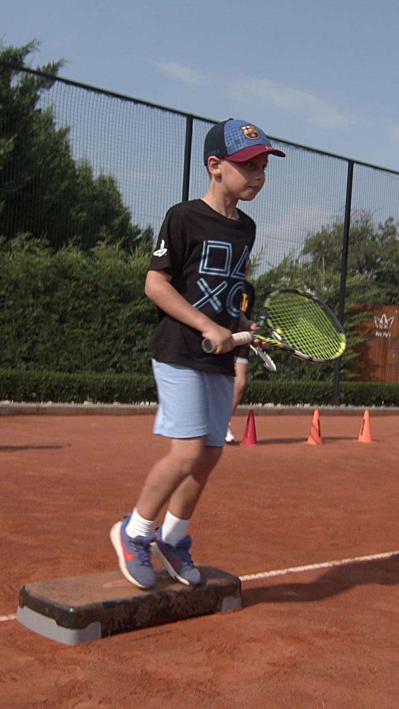 Дете тренира тенис на клей корт в NOVI Tennis Club — детски тренировки в Пловдив